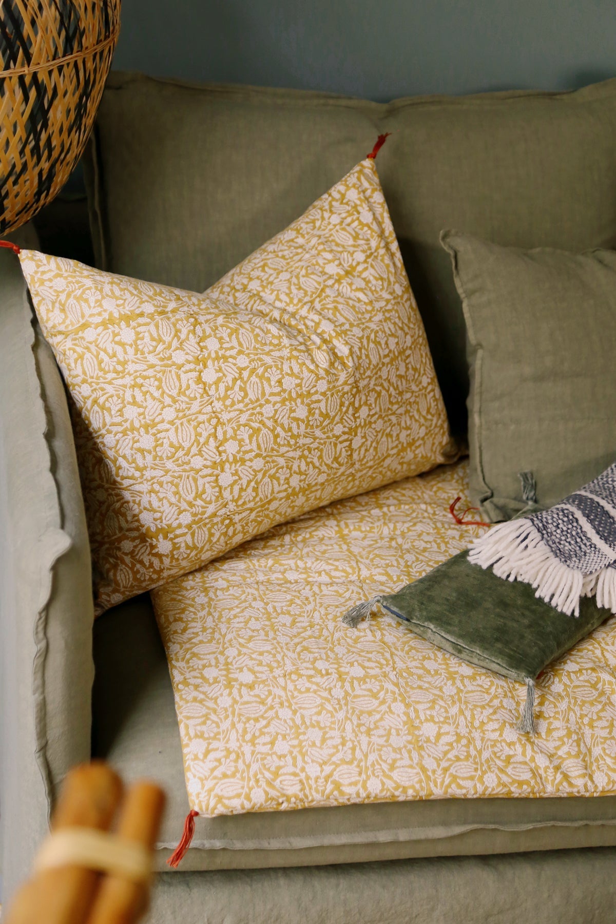 Housse de coussin Tulipan à motifs Curcuma sur un canapé vert