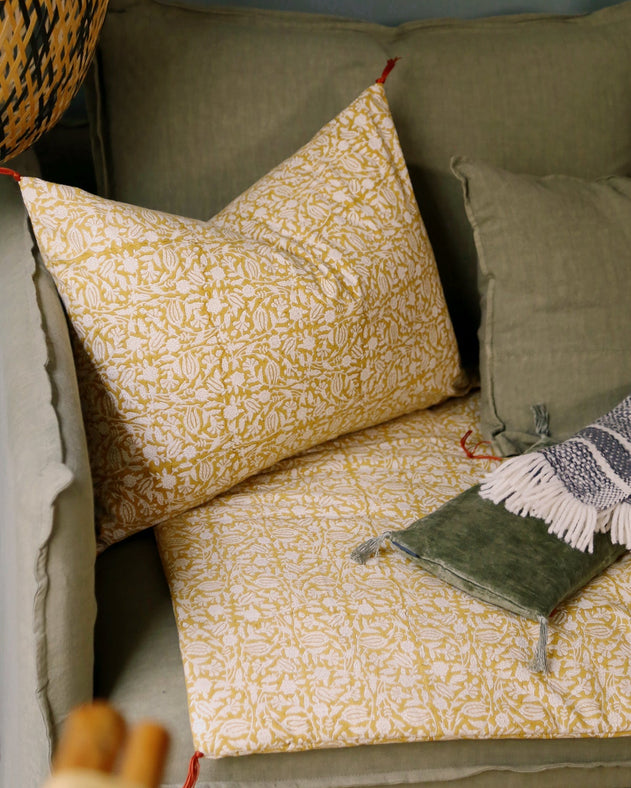 Housse de coussin Tulipan à motifs Curcuma sur un canapé vert