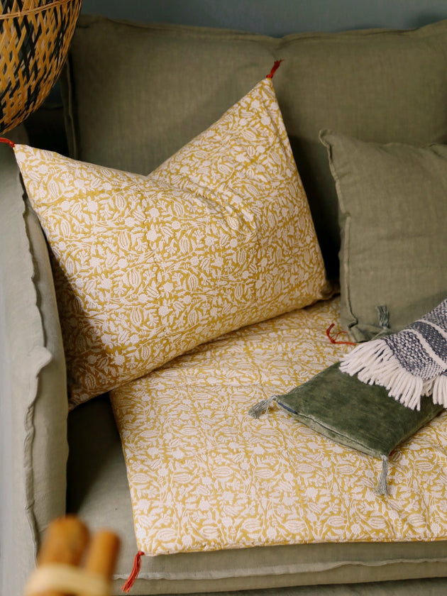 Housse de coussin Tulipan à motifs Curcuma sur un canapé vert