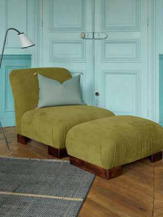 La chauffeuse Pacha et son repose-pieds à la structure en hêtre massif et au tissu en lin Gareth dans un salon élégant. 