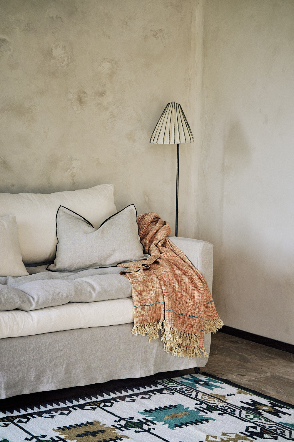 Housse de coussin Maya en lin sauvage avec bourdon noir au pourtour idéale sur un canapé.