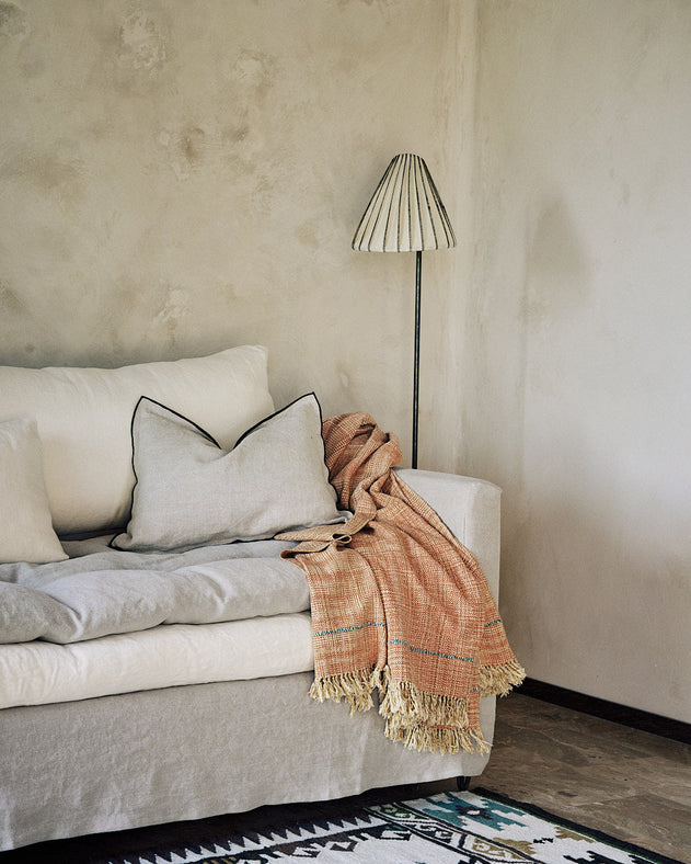 Housse de coussin Maya en lin sauvage avec bourdon noir au pourtour idéale sur un canapé.
