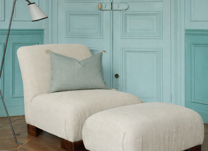 La chauffeuse Pacha et son repose-pieds à la structure en hêtre massif et au tissu en lin Gareth dans un salon élégant. 