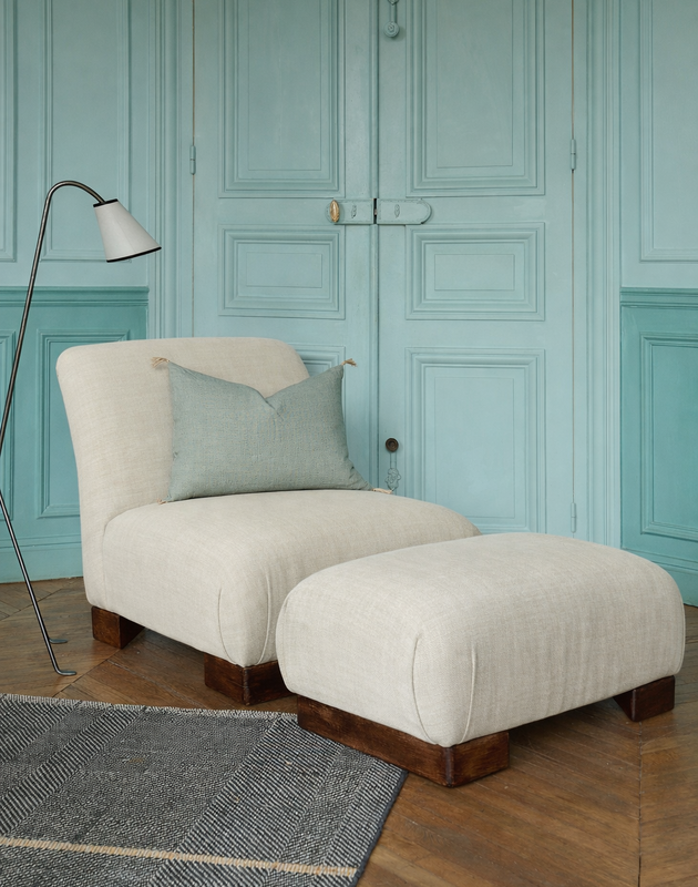 La chauffeuse Pacha et son repose-pieds à la structure en hêtre massif et au tissu en lin Gareth dans un salon élégant. 